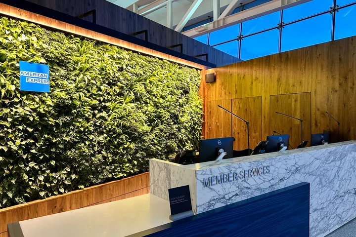 American Express Centurion Lounge member services desk with living green wall and Amex logo.