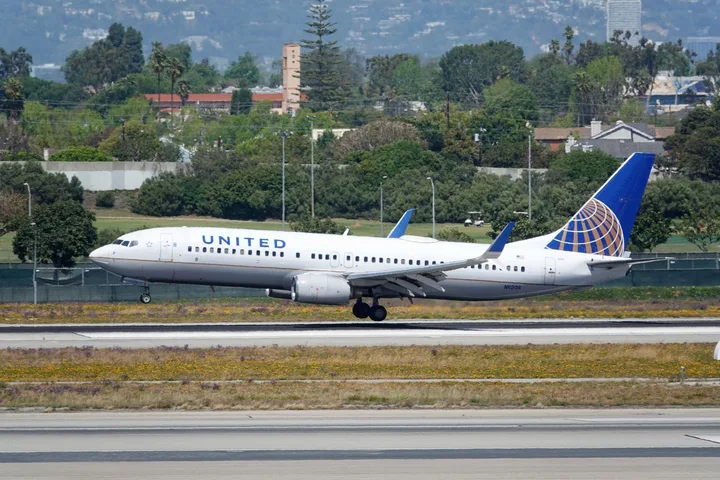 United Airlines Boeing 737 taxiing on runway with green suburban backdrop.