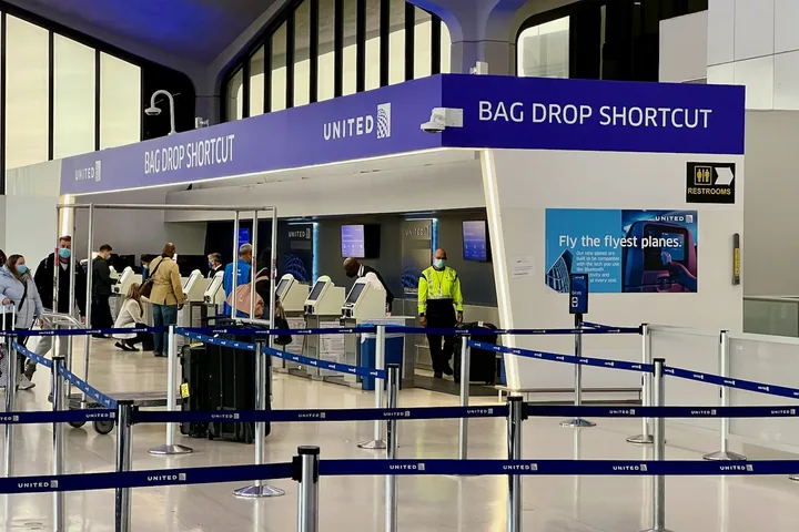 United Airlines Bag Drop Shortcut counter with passengers and queue barriers in terminal.