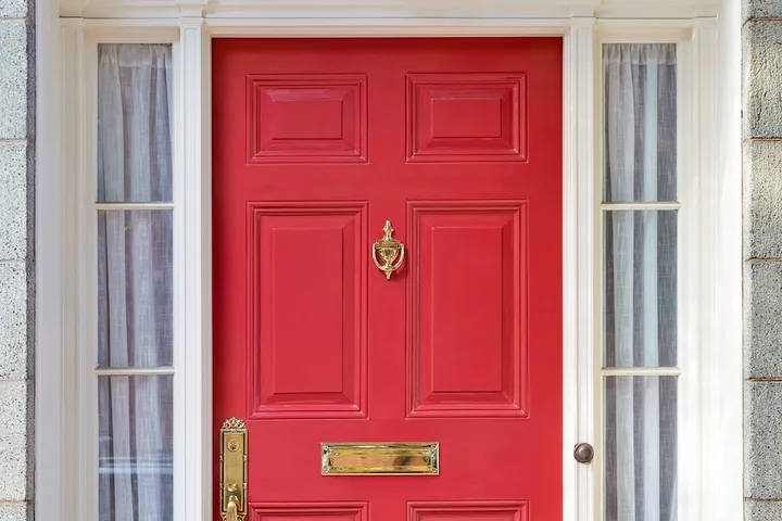 Bold red six-panel front door with brass knocker and mail slot on stone house.