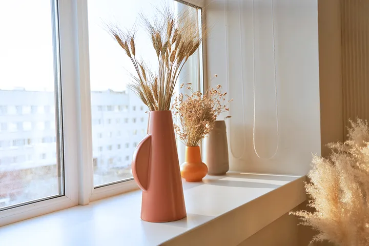 Decorative vases with dried grasses arranged on a sunny window sill.
