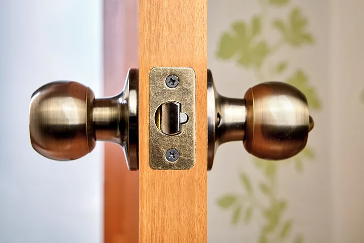 Close-up of antique brass door knob and latch mechanism on a wooden door.