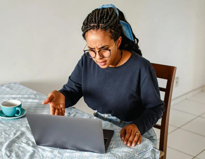 Woman with glasses looking frustrated or confused at a laptop on a kitchen table.
