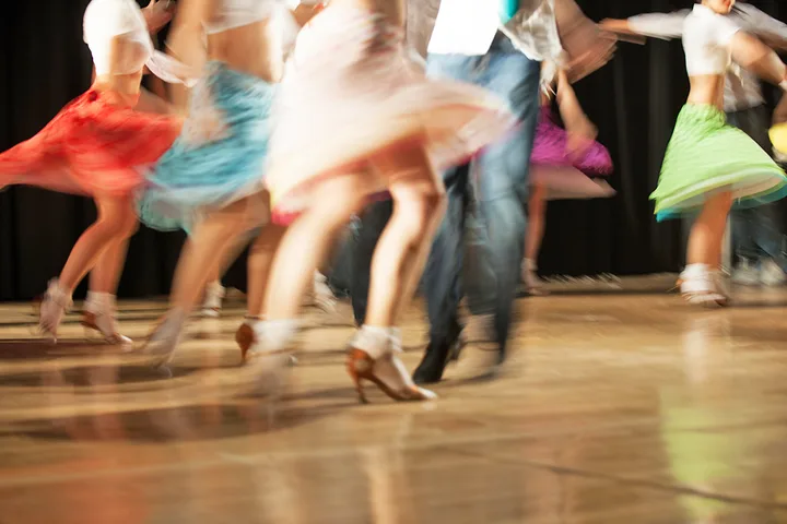 Blurred motion shot of dancers in colorful skirts spinning on a dance floor.