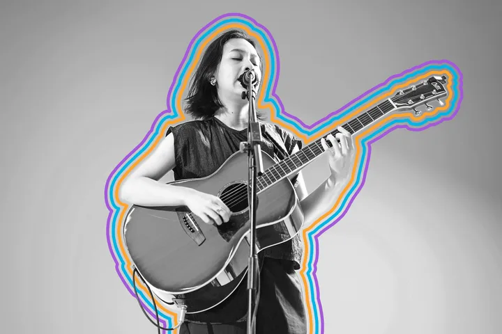 Black-and-white photo of a woman singing and playing acoustic guitar at a microphone.