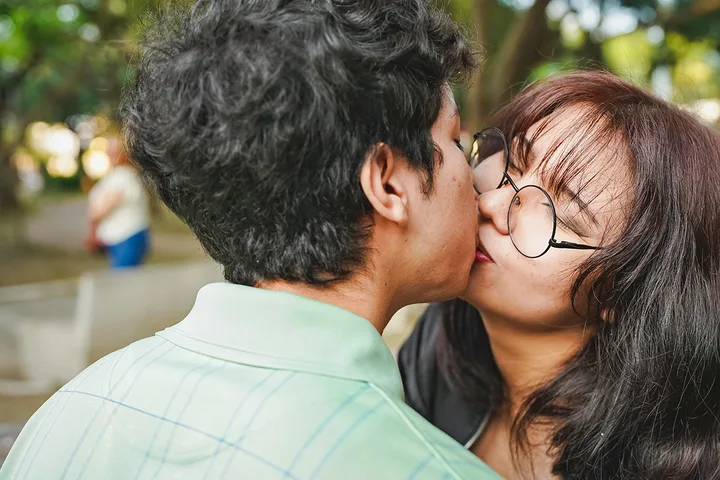 Young couple sharing a kiss outdoors in a park setting.