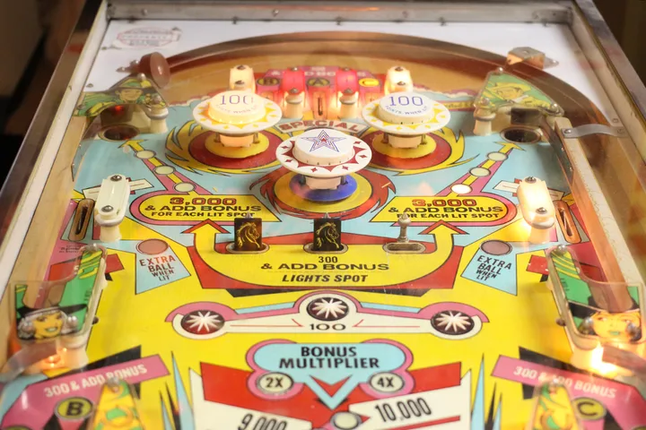 Close-up of a vintage pinball machine playfield with colorful artwork and bumpers.