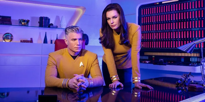 Two actors in gold Star Trek uniforms posed together in a futuristic command room.