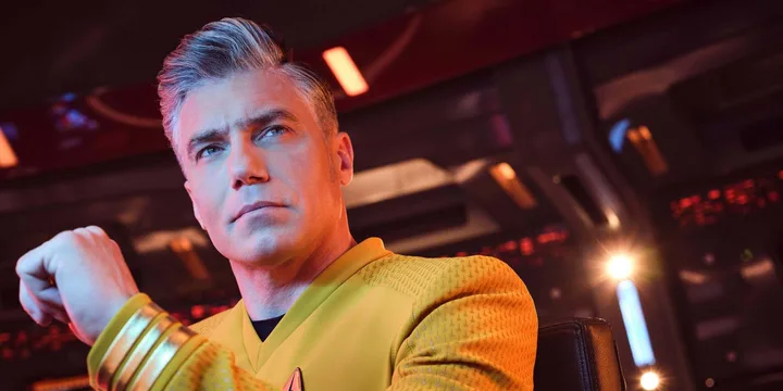 Close-up of male actor in gold Star Trek captain's uniform on a lit bridge set.