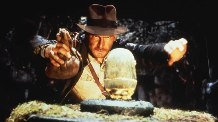 Harrison Ford as Indiana Jones reaching for a golden idol in a dark cave.