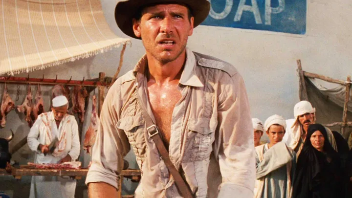 Harrison Ford as Indiana Jones standing alert in a Middle Eastern market scene.