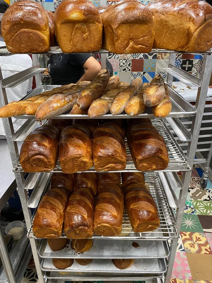 Bakery rack loaded with freshly baked loaves and baguettes, with a worker visible in background.