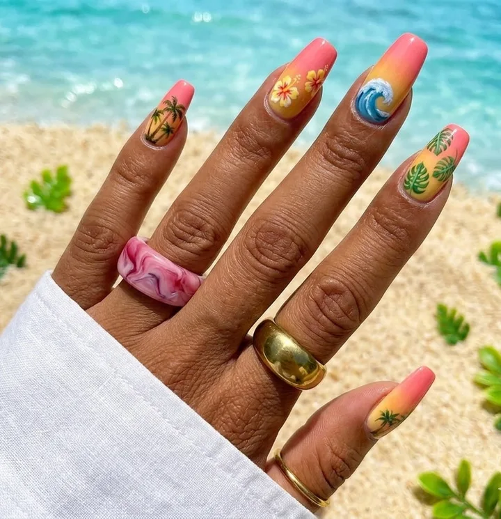 Hand with tropical nail art featuring palm trees, hibiscus, waves, and monstera leaves at a beach.