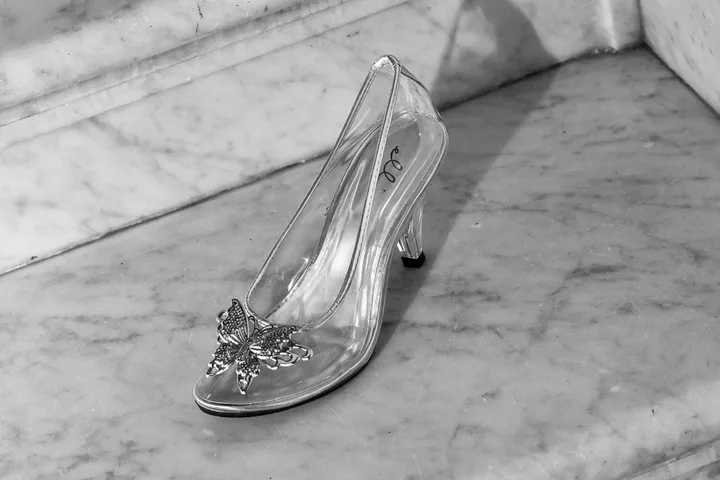 A clear glass slipper with butterfly embellishment resting on marble steps, black and white photo.