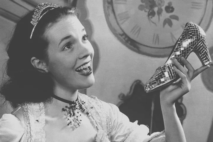 Black and white vintage photo of a young woman in tiara holding a glittering high-heel shoe.