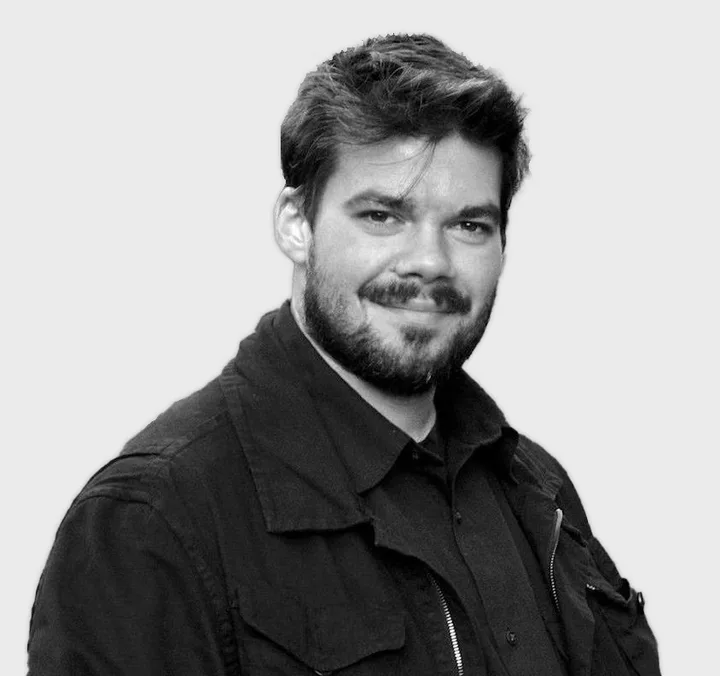 Black and white headshot of a young bearded man in a dark jacket against a plain background.