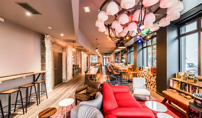 Stylish hostel common room with red sofas, pendant lights, bar stools, and open layout.
