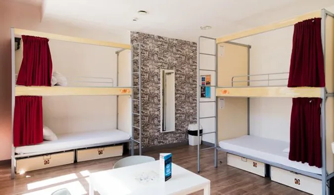 Clean hostel dorm room with metal bunk beds, red curtains, and Paris-themed wallpaper.