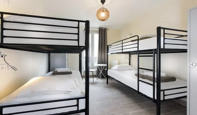 Minimalist hostel dorm room with black metal bunk beds, white linens, and natural light.