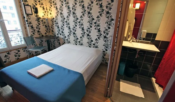 Small private hostel room with a single bed, floral wallpaper, and ensuite bathroom visible.