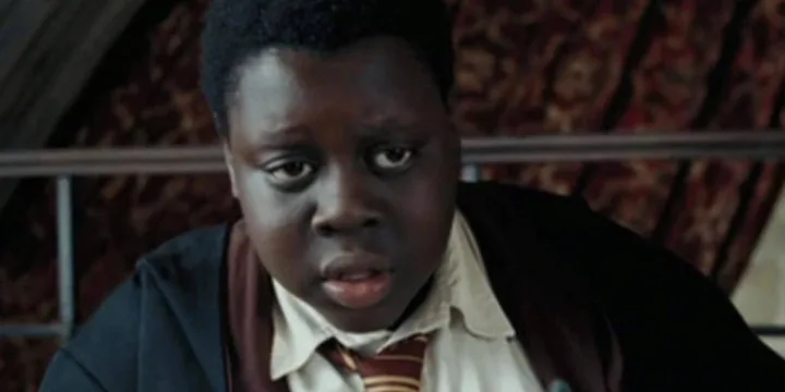 Young Black boy in Hogwarts uniform with a surprised expression in a dimly lit scene.