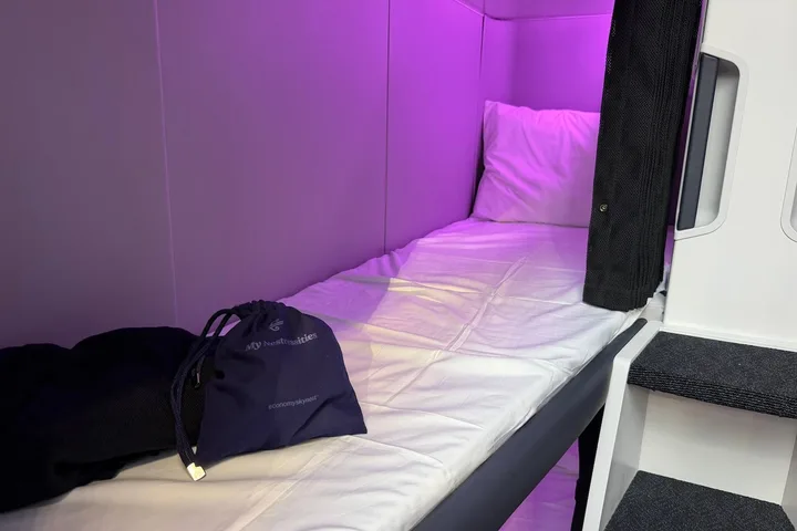 Close-up of a single Air New Zealand Skynest sleep pod with white mattress, pillow, and purple ambient lighting.