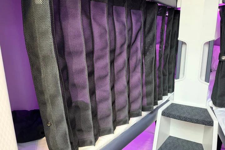 Close-up of dark mesh privacy curtains partially closed on Air New Zealand Skynest sleep pods with purple lighting behin