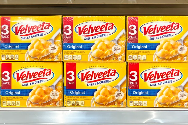 Six boxes of Velveeta Shells & Cheese stacked on a store shelf.