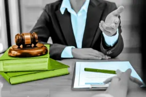 A lawyer at a desk gestures toward documents, with a gavel and law books in foreground.